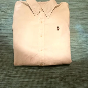 Vit skjorta från Ralph Lauren - Klassisk vit skjorta från Ralph Lauren med button-down krage och broderad logga på bröstet. Skjortan har lång ärm, knappar framtill och är tillverkad i mjuk bomull. Skjortan är slim-fit.  Perfekt för en clean och stilren look. 