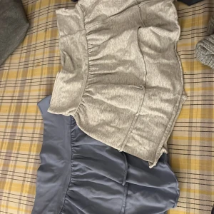 Två volangkjolar från H&M, grå & blå - Säljer två snygga volangkjolar från H&M. En är ljusgrå i mjuk bomull och den andra är blå med satinliknande yta. Båda är korta och har bred volangkant som ger en trendig look. Perfekta för dig som gillar en feminin och chill stil.  Frakt till kommer 