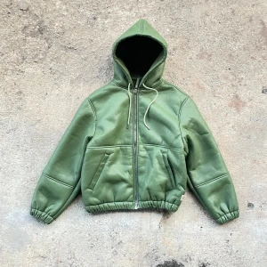 Grön Stüssy skinnjacka   - Säljer en grön skinnjacka från Stüssy med huva och mysigt teddyfoder. Jackan är i helt nytt skick  och priset kan även gå att diskuteras