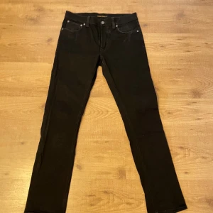 Svarta jeans från Nudie Jeans - Svarta jeans från Nudie Jeans med klassisk femficksdesign och diskreta sömmar på bakfickorna. Jeansen har en smal passform och är tillverkade i ett mjukt bomullstyg med stretch. Perfekta för dig som gillar stilrena och bekväma jeans.