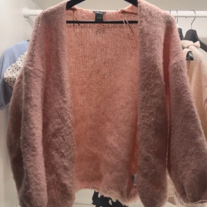 Rosa fluffig kofta från Lindex - Supermjuk och oversized rosa kofta från Lindex. Koftan är stickad med en fluffig känsla, har långa ärmar och öppen front utan knäppning. Perfekt för lager-på-lager och ger en mysig vibe till din outfit.