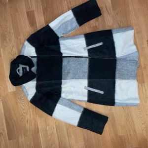 Randig lång jacka från Vila - Säljer en lång, randig jacka från Vila i svart, grått och vitt. Jackan har dragkedja framtill, två fickor och klassisk krage. Materialet känns mjukt och lite ulligt, perfekt för kyliga dagar. Snygg och stilren design som sticker ut.