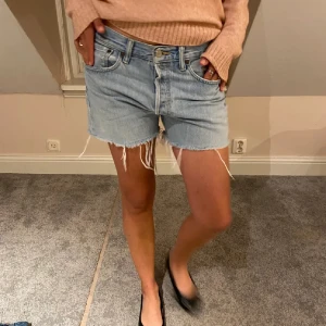 Levi's ljusblå jeansshorts med fransar - Ljusblå jeansshorts från Levi's med klassisk femficksdesign, råa fransiga benslut. Shortsen har en avslappnad passform och tydliga Levi's-detaljer som läderpatch och röd etikett bak. Som ni ser på sista bilden finns det ett litet hål därav är priset lägre och går även att sy ihop enkelt! 🌸