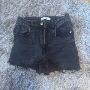 Svarta jeansshorts Gina - Snygga svarta jeansshorts från Gina i storlek M. De har hög midja, råa fransiga kanter och klassisk femficksdesign. 