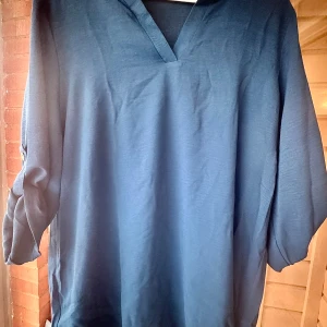 Blå blus med knappdetalj XXL - Säljer en blå blus i XXL. 100% polyester med v-ringning och trekvartsärmar som har snygg knappdetalj. Blusen har en loose passform och är perfekt för dig som gillar en enkel men stilren look. 