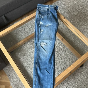 Replay jeans - Säljer ett par blå jeans från Replay med slitna detaljer och snyggt tvättad look. Klassisk femficksmodell med dragkedja och läderpatch bak. Jeansen är modellen anbass och är i storlek 33/34