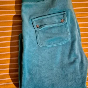 Turkosa mjukisbyxor med snörning - Säljer ett par turkosa mjukisbyxor med bred resår i midjan och snörning framtill. Byxorna har en stor ficka med lock och knapp på sidan, vilket ger en chill och sportig vibe. Perfekta för att hänga hemma eller dra till promenad 