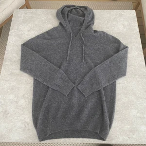 Mörkgrå hoodie i merinoull  - Mysig mörkgrå hoodie i merinoull med huva och dragsnören. Tröjan har lång ärm och ribbade muddar vid ärmslut och nederkant. Perfekt för kyliga dagar när du vill vara både bekväm och snygg.