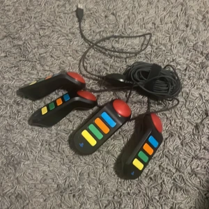 Buzz! Buzzers för PlayStation 2 - Fyra original Buzz! buzzers för PlayStation 2. Perfekt för partyspel och quiz. Färgglada knappar, USB-anslutning. Alla knappar syns hela och i gott skick, mindre repor kan förekomma men inget som påverkar funktionen.