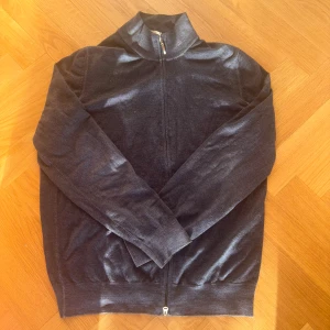 Gran Sasso svart kofta med dragkedja - Svart kofta från Gran Sasso med hel dragkedja och ribbade muddar. Tillverkad i Italien, klassisk och stilren design med hög krage. Perfekt för lager-på-lager och funkar året runt. Materialet känns mjukt och lätt, troligen bomull eller ullblandning. Nypris: 5500kr