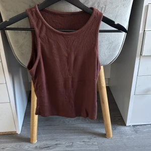 Ribbad brun linnetopp - Säljer en ribbad brun linnetopp med rund halsringning. Toppen är ärmlös och har en enkel, stilren design som passar perfekt till jeans eller kjol. Materialet är mjukt och stretchigt för en bekväm passform.
