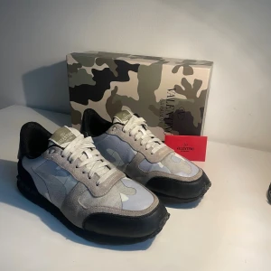 Valentino Rockrunner sneakers - Snygga Valentino Rockrunner sneakers med vitt och ljusblått camouflagemönster, svarta detaljer och vita skosnören. Box samt Valentino kort medföljer. Ovandel i mocka och textil, svart sula med nitar vid hälen. Perfekta för dig som vill sticka ut med stilrena och exklusiva sneakers. Perfekt till höst och vintern! 