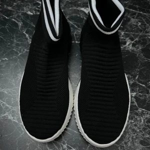 Svarta sock-sneakers med vit sula - Säljer ett par svarta sock-sneakers med ribbad stickad ovandel och högt skaft. Skorna har en vit, vågformad sula och svart-vit rand runt skaftet. Perfekta för dig som gillar sportig och modern stil.