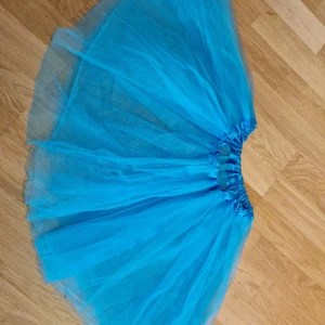 Blå tyllkjol med volym - Säljer en superfin blå tyllkjol med mycket volym och resår i midjan. Kjolen är kort och har flera lager tunn tyll som ger en fluffig och lekfull look. Vår dotter hade den till en ballerinadräkt. Står ingen storlek i plagget men ca 4-7 års ålder är en kvalificerad uppskattning.