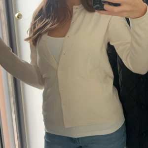 Beige kofta med knappar - Snygg beige kofta med rund halsringning och knäppning framtill. Långärmad och i mjukt material, perfekt att slänga över ett linne eller t-shirt. Enkel och stilren design som passar till jeans eller kjol.