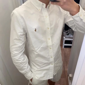Polo Ralph Lauren (Vit skjorta) - Säljer en klassisk vit skjorta från Polo Ralph Lauren. Skjortan har långa ärmar och knappar framtill. Perfekt för en stilren look. Den är i underbar skick och redo för en ny ägare! Skjortan är size L men passar även M!