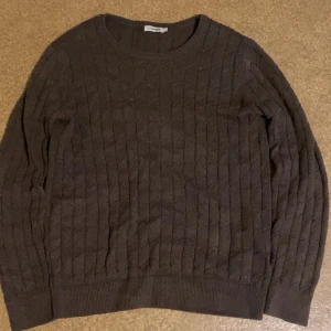 Mörkbrun stickad tröja J.Lindeberg - Säljer en mörkbrun stickad tröja från J.Lindeberg med snyggt strukturmönster. Tröjan har rund halsringning, långa ärmar och ribbade muddar vid ärmslut och nederkant. Perfekt för kyliga dagar och enkel att matcha med jeans.
