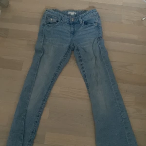 Blå jeans från Gina Tricot, stl 158 - Snygga ljusblå jeans från Gina Tricot i storlek 158. Klassisk femficksmodell med liten bootcut ben och knappstängning. Jeansen har bälteshällor och bakfickor med lock och knapp. Perfekta för en avslappnad och trendig look.