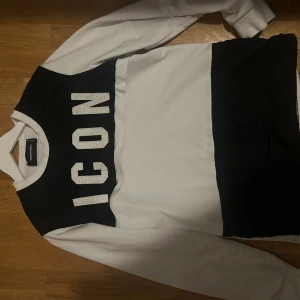 Svartvit sweatshirt från Dsquared2 ICON - Säljer en svartvit sweatshirt från Dsquared2 med stor 'ICON'-text framtill. Tröjan har breda blockfärger, rund hals och långa ärmar. Tillverkad i mjuk bomull, perfekt för en cool och avslappnad stil.