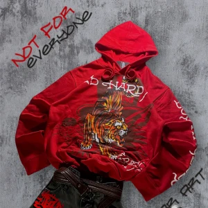 Röd Ed Hardy hoodie med tigertryck - Snygg röd hoodie från Ed Hardy med fet tigerprint på bröstet och coola vita tryck på ärmarna. Klassisk huva med dragsko och känguruficka framtill. Perfekt statement-plagg för dig som vill sticka ut.