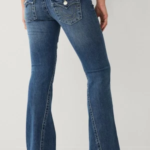 True Religion Joey Low Rise Flare Jeans - Säljer ett par blå True Religion Joey jeans med låg midja och utsvängda ben. Klassiska kontrastsömmar, snygga bakfickor med lock och guldiga knappar. Jeansen är i denim och har en riktigt ikonisk 2000-talsvibe.