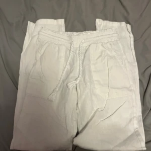 Vita linnebyxor från Skagen  - Säljer ett par fräscha vita linnebyxor med elastisk midja och snörning. Byxorna har avslappnad passform och stora fickor framtill. Perfekta för en chill och stilren look under varma dagar.