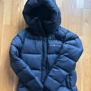 Svart dunjacka Sail Racing dam XS - Säljer en svart pufferjacka från Sail Racing, modell W Cloud Down Hood. Jackan har en rejäl huva, dragkedja framtill och är fylld med certifierat ankdun (700 fill power). Yttermaterialet är nylon och jackan är perfekt för kalla vinterdagar.