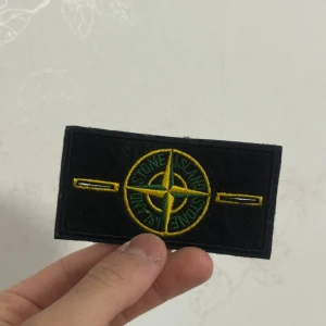 Klassisk Svart/Gul Kompass - Originalinspirerad S I badge i svart med gul/grön kompass. 	•	Kan enkelt fästas på jackor, tröjor eller väskor 	•	Ikonisk detalj för en unik look 	•	Perfekt som extra patch eller ersättning 