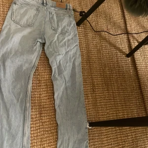 Ljusblå raka jeans med råa kanter - Ljusblå jeans med raka ben och råa, fransiga kanter nertill. Jeansen har klassisk femficksdesign och slitningar på ena benet för en avslappnad vibe. Perfekta för dig som gillar en chill och trendig look.