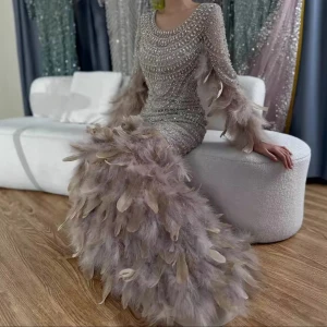 Champagnefärgad långklänning med fjädrar - Kan mötas i Stockholm ifall du vill kolla på den innan köp! Använd en gång, Superglammig långklänning i champagnefärg med glittriga pärldekorationer och massor av fjädrar på ärmar och kjol. Klänningen har rund halsringning, långärmad design och figurnära passform. Perfekt för dig som vill sticka ut och glänsa på bal eller fest.