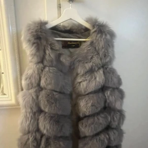 Grå pälsväst från RuiXiangFe - Fluffig och lyxig grå pälsväst från RuiXiangFe. Västen har en voluminös look med breda, horisontella sektioner och är ärmlös. Perfekt för att ge din outfit en extra edge under kyliga dagar.PRISET KAN DISKUTERAD, STORLEKEN ÄR 36, Går bra för M och L, kvaliteten är jätte bra, fin.
