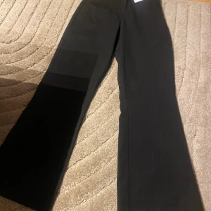 Svarta vida byxor i storlek 36 - Svarta byxor från Tammy i storlek 36. Byxorna har en rak och vid passform med klassisk look och är tillverkade i ett mjukt tyg som känns bekvämt. Perfekta för dig som gillar en stilren och enkel vibe.