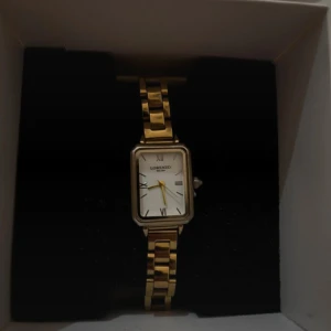 Guldig fyrkantig klocka Lorenzo Milano - Stilren klocka från Lorenzo Milano med fyrkantig urtavla i vitt och romerska siffror. Armbandet är i guldtonad metall med klassisk länkdesign. Perfekt accessoar för dig som gillar en elegant och tidlös look. Nytt skick 