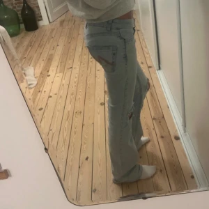 Ljusblå slitna jeans med hål på knäna - Säljer ett par ljusblå jeans med raka ben och snygga hål på båda knäna. Jeansen har klassisk femficksdesign och låg midja. Perfekta för en avslappnad och trendig look.