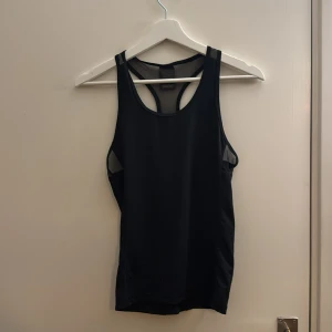 Svart sportlinne från Energetics - Svart sportlinne från Energetics med meshdetaljer i ryggen och vid sidorna för extra ventilation. Linnet har en racerback-modell och är gjort i ett stretchigt syntetmaterial och är löst sittande