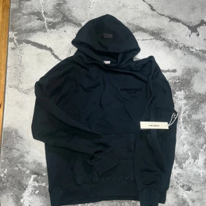 Svart Essentials Fear of God hoodie - Svart Essentials Fear of God hoodie i streetwear-stil. Oversized passform med tryck fram och bak. Passar M, L och XL – lite beroende på hur du vill att den sitter.