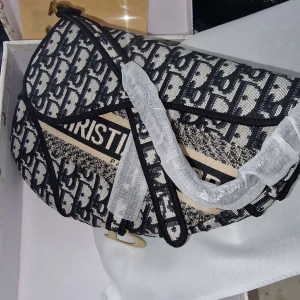 Dior Saddle Bag i blått mönster - Säljer en ikonisk Dior Saddle Bag med blått och beige monogrammönster, guldfärgade metalldetaljer och klassisk sadelform. Väskan har broderad logga och justerbar axelrem. Perfekt statement piece för dig som vill sticka ut.