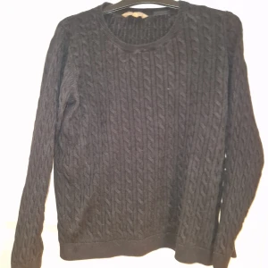 Svart kabelstickad tröja - Kabelstickad svart tröja med rund hals och långa ärmar. Tröjan har ett klassiskt mönster och är perfekt för dig som gillar en enkel men snygg look. Passar till jeans eller chinos och är riktigt skön under kyliga dagar.