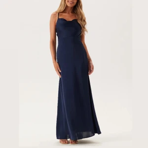 Marinblå mörkblå balklänning långklänning med öppen rygg - Snygg marinblå långklänning i satinliknande material med smala reglerbara axelband och djup v-ringning i ryggen. Klänningen har en elegant, figurnära passform upptill och faller snyggt längs kroppen. Den passar perfekt till studentbal, och är endast använd en gång på min studentbal ifjol. 