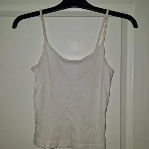 Vit ribbad linnetopp med smala band - En basic vit ribbad linnetopp med smala axelband. Enkel och stilren modell som passar perfekt till jeans eller shorts. Mjuk och stretchig känsla, perfekt för varma dagar.