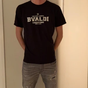 T-shirt - Svart t-shirt från BVALDI med collegeinspirerat vitt tryck på bröstet där det står 'College League BVALDI Champions Since 2021'. Klassisk rund hals och normal passform. Perfekt för en avslappnad och sportig stil.