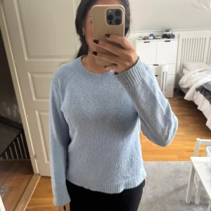 Ljusblå stickad tröja med rund hals - Mysig ljusblå stickad tröja med rund halsringning och ribbade muddar vid ärmslut och nederkant. Tröjan har en klassisk passform och långa ärmar, perfekt för lager-på-lager under kyliga dagar.