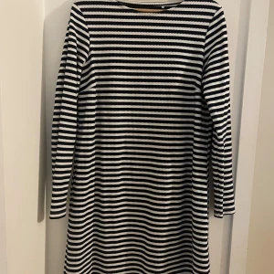 Randig klänning Holly & Whyte - Superfin klänning från Holly & Whyte med marinblå och vita ränder. Klänningen har lång ärm med snygga guldiga knappar vid ärmsluten och är gjord i ett mjukt, stickat material. 