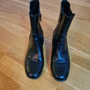 Svarta chelsea boots i skinn - Snygga svarta chelsea boots i skinn med dragkedja på insidan och elastiska paneler på sidorna. Boots med fyrkantig tå och låg klack, perfekta för en stilren look. Klassisk design som funkar till många outfits.