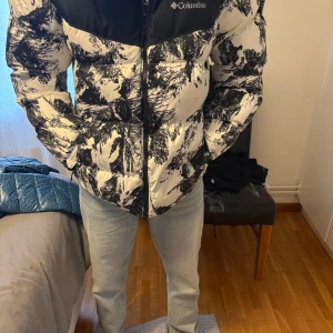 Svartvit pufferjacka från Columbia M - Säljer en fet pufferjacka från Columbia i storlek M. Jackan är svart och vit med ett unikt abstrakt mönster, har huva och dragkedja framtill. Perfekt för kalla dagar och riktigt snygg streetstil. Insidan har coolt mönstrat foder.