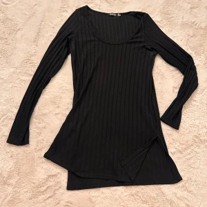 Svart långärmad topp med slits  - Svart långärmad topp från Boohoo i ribbad polyester med rund hals och slits i nederkant. Snygg, slim passform och diskret randigt mönster. 