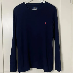 Ralph Lauren tröja  - Säljer en stilren mörkblå långärmad tröja från Ralph Lauren. Tröjan har en liten röd logotyp på bröstet och är tillverkad i ett bekvämt material. Perfekt för en avslappnad stil.