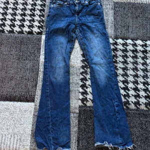 True Religion blå bootcut jeans - Säljer ett par blå jeans från True Religion med bootcut passform . Klassiska fickor med lock och synliga sömmar bak, samt logga på bakfickan. Jeansen har låg midjan. Dom är insydda i benen och har ett lite hål mellan benen men det är bara o sy ihop så syns det inte. Är storlek w 27 men passar 26
