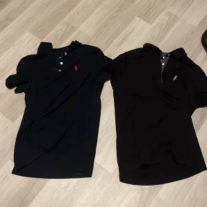 Två svarta pikétröjor från Polo Ralph Lauren - Säljer två klassiska svarta pikétröjor från Polo Ralph Lauren. Ena har röd broderad logga och den andra har vit logga. Båda har krage, knappar framtill och korta ärmar. Perfekta för en clean och stilren look.  420 för båda