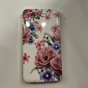 Powerbank med blommönster - Stilren powerbank från Ideal of Sweden med vackert blommönster och guldfärgade kanter. Utrustad med USB och USB-C-port. Mycket gott skick, inga synliga repor eller skador. Perfekt accessoar för att ladda mobilen med stil.